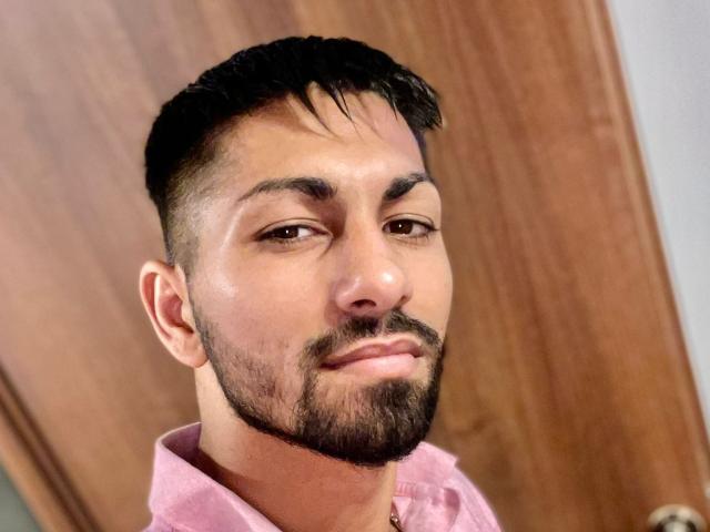 NigelBoydX has a short, dark, well-groomed beard and mustache, with a slightly serious expression, wearing a pink shirt, and a close-cropped, dark hairstyle.