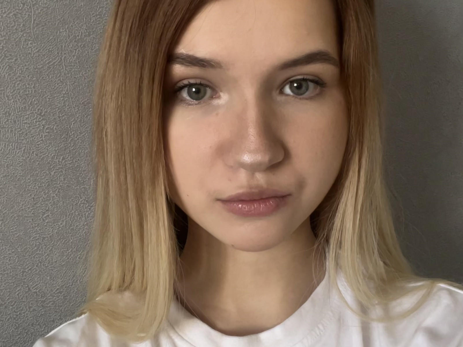 NubiaErspamer has blonde hair, green eyes, and a neutral expression. She's wearing a white shirt, and her face is centered in the image.