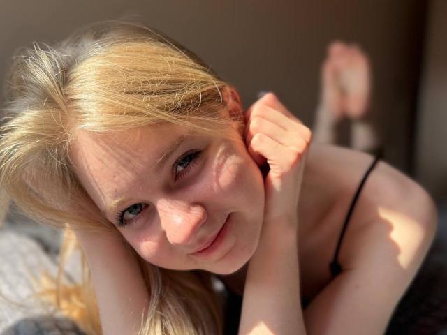 Susan Nickeson met blond haar, lachend, zonlicht op haar gezicht, zwarte bandjes, handen op haar hoofd, zachte schaduwen, onbedekte schouders, lichte huid, ontspannen, zachte uitdrukking, casual, close-up, natuurlijk licht..