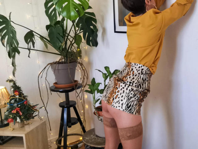 LaPhoenixElo stands with her back to the camera, wearing a yellow shirt, leopard print shorts, and lace-topped thigh-highs, her ass and brown lace garter visible.