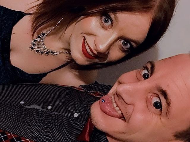 CoupleCadresPervertis with red lipstick, blue eyes, and silver necklace, smiling. Bald CoupleCadresPervertis with tongue out, blue nose piercing, and striped shirt.