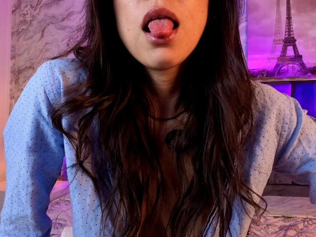 MiaReed's face, tongue out, wearing a blue polka dot shirt, long wavy brown hair, visible cleavage, purple and blue lighting, Eiffel Tower in the background.