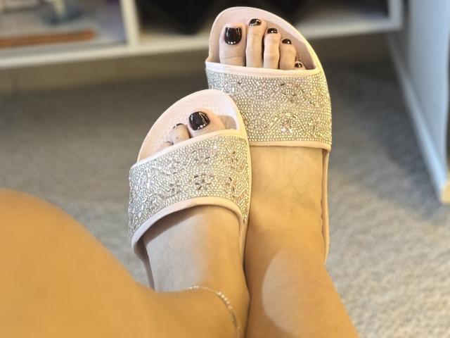 KatherineToro's feet in sparkly silver open-toe heels, showing black-painted toenails, with a delicate ankle bracelet, resting on a carpeted floor.
