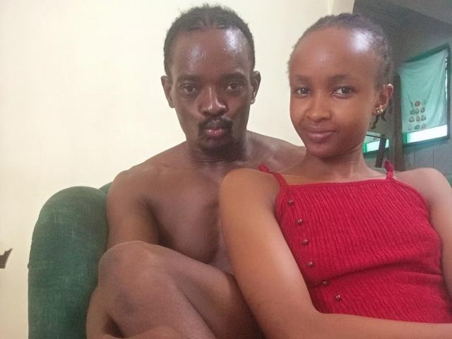 Two HoneyBadgers sitting on a green couch. The HoneyBadger on the left is shirtless with dark skin and short hair, while the HoneyBadger on the right wears a red top.