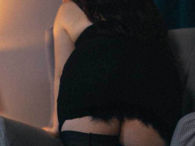 EffyRain's butt in black lace underwear, slightly pulled down, showing a hint of skin, sitting on a gray chair, with long dark hair falling down her back.