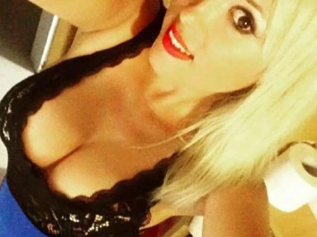 SilviaHot-hot with blonde hair, red lipstick, and black lace top showing her big boobs, smiling at the camera. Her cleavage is prominent and she's wearing blue.