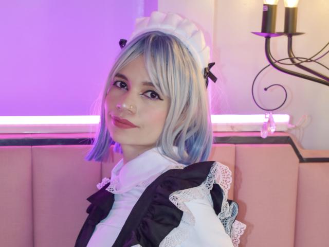 SofiArias with blue and white bob, black and white maid outfit, lace trim, black ribbons, nose ring, purple and pink lighting, looking over shoulder, cute, pink cushion.