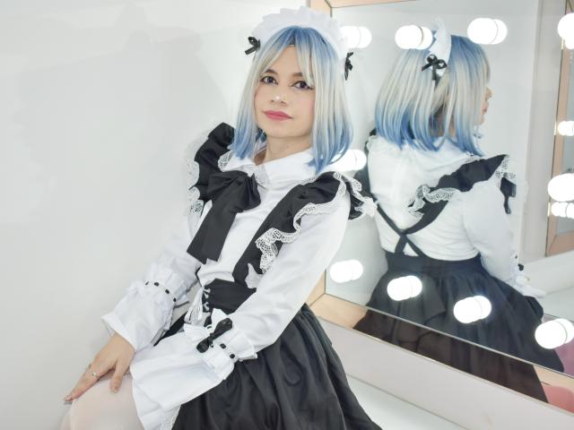 SofiArias with blue and white hair, wearing a black and white maid outfit, sitting in front of a mirror with light bulbs, showing her back and ass.