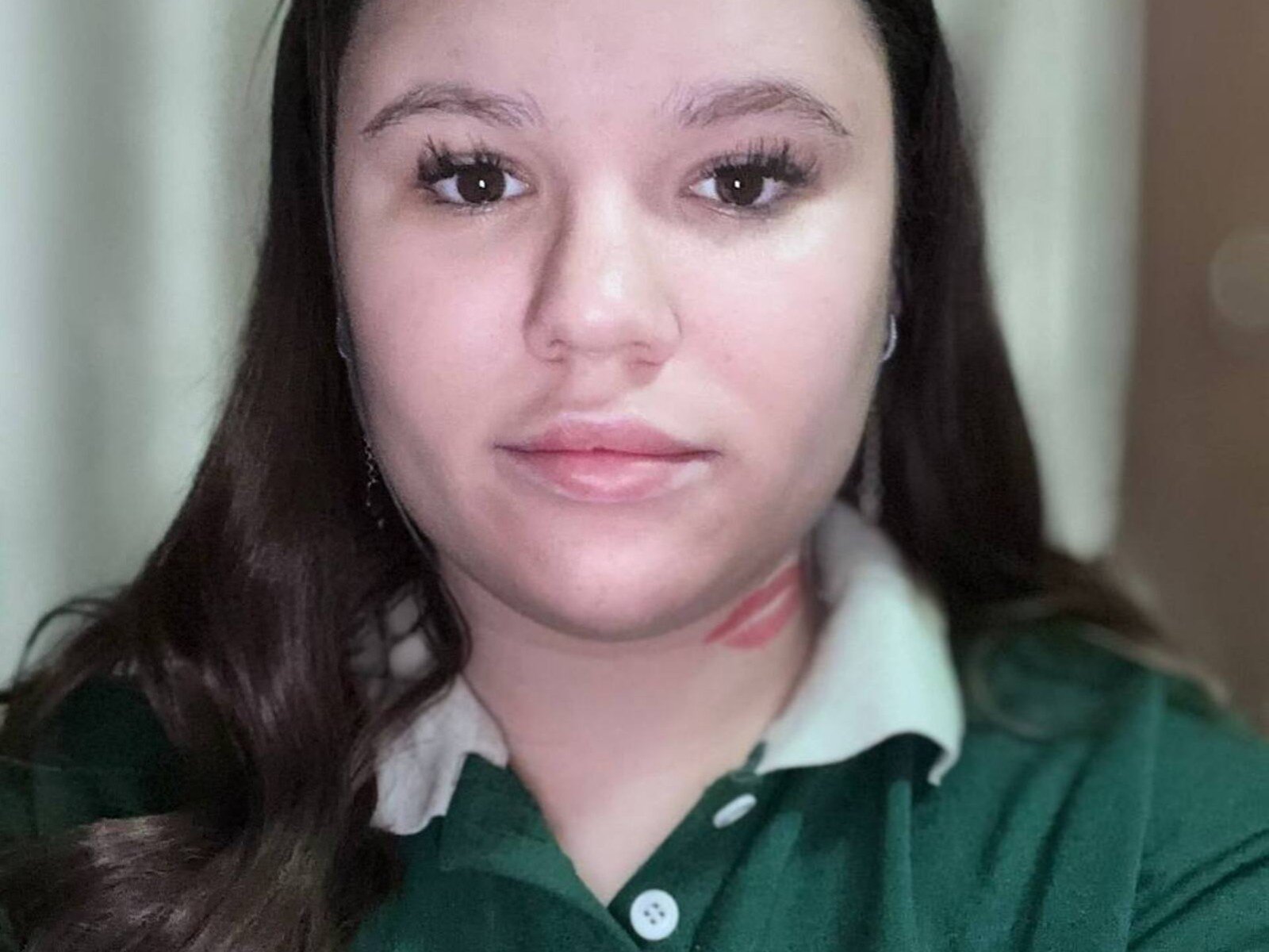 HedwigSkill has fair skin, brown eyes, and long dark hair, wearing a green polo shirt with a white collar. She's looking straight at the camera with a slight smile.
