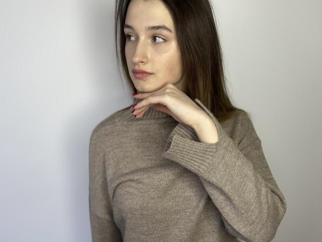 CharleenTilton with light skin, brown hair, and red nails, wearing a gray turtleneck, her hand gently touching her chin, looking to the side with a subtle, confident expression.