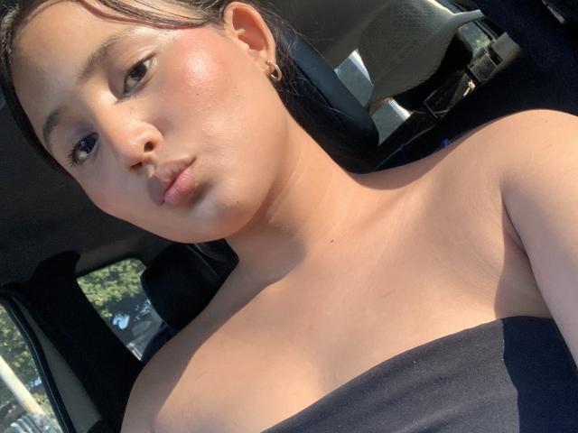 Ximenitax has a cute face with pinkish cheeks, brown eyes, and black hair. She's wearing a black strapless top, showing her bare shoulders and small tits.