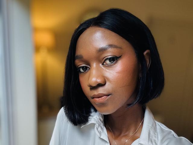 Mysteryslady has shiny black bob, brown eyes, subtle winged eyeliner, smooth brown skin, white shirt, and a gentle smile with slightly parted lips. She's looking directly at the camera.