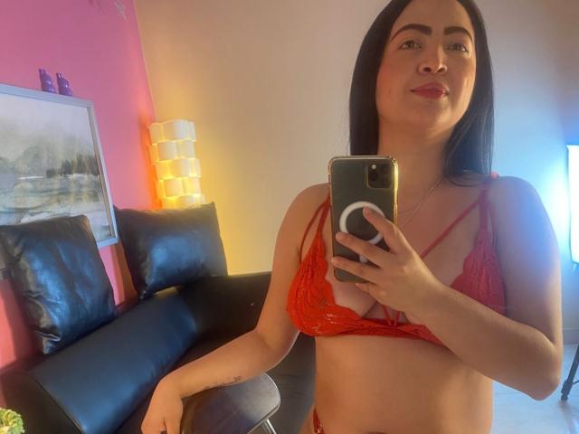 AlanaWest with long black hair, red lace bra, and matching panties, taking a mirror selfie, showing her tits and small ass, smiling with red lipstick.