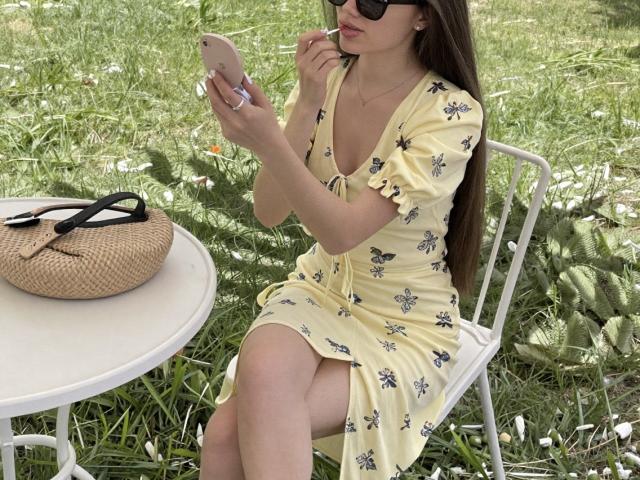 Euphorias, with tits partially visible in a yellow butterfly dress, sits on a white chair, texting on a rose gold phone, wearing black sunglasses, and holding a straw.