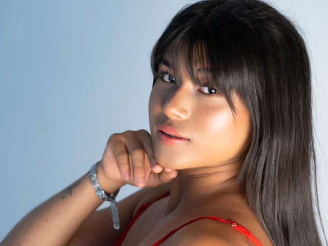 AshlyLee has dark brown hair, red lips, and is looking at the camera with her hand near her chin. She's wearing a red bra and a silver bracelet.