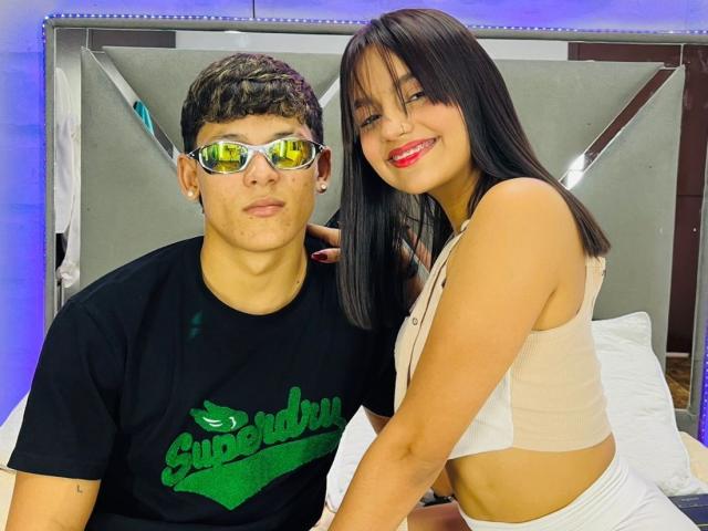 EndlessTwo with short brown hair and glasses, wearing a black Superbad shirt, sits next to EndlessTwo with long black hair, red lipstick, and a beige sports bra, smiling.