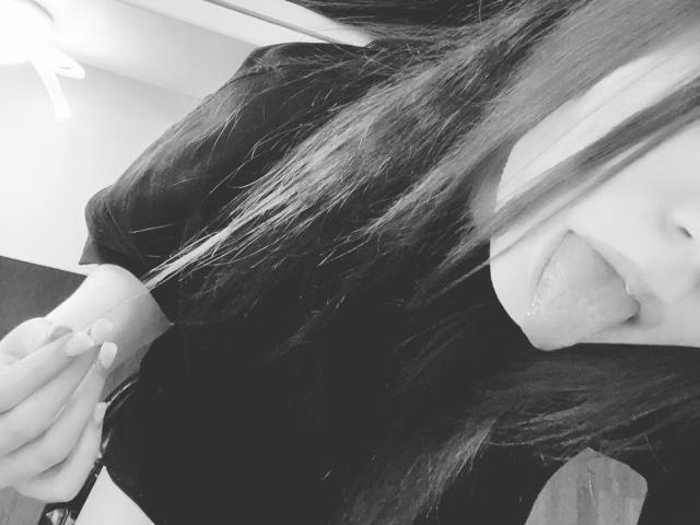 Selfie en blanco y negro de FarahCantre con cabello largo, sacando la lengua, vistiendo una camisa negra, mostrando una mano con uñas manicuradas y una vista parcial de sus senos..