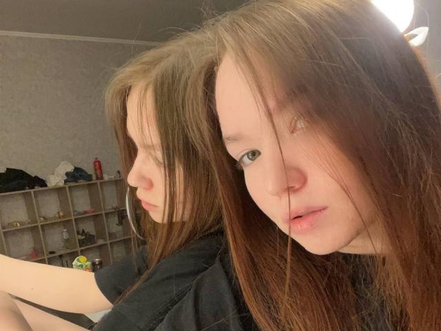 FarahCantre has long brown hair, pale skin, and green eyes, staring into a mirror with her reflection showing her side profile. She's wearing a black shirt.