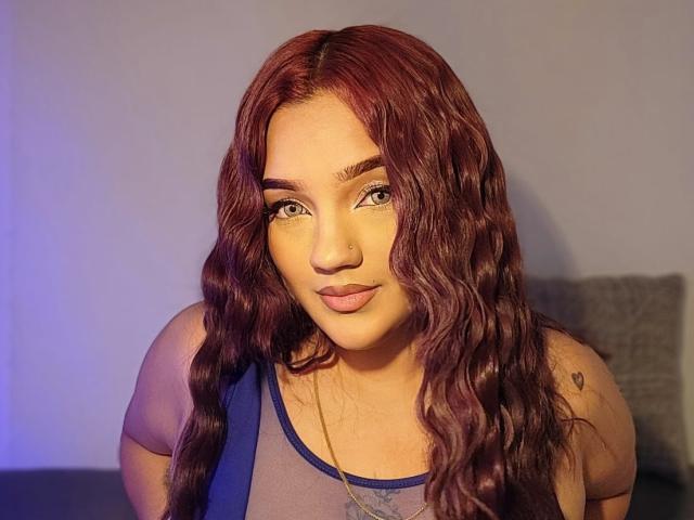 Valerie Wet tiene el pelo rojo ondulado, ojos verdes y un piercing en la nariz muy bonito. Lleva una blusa azul transparente con un pequeño tatuaje de corazón en el hombro derecho..
