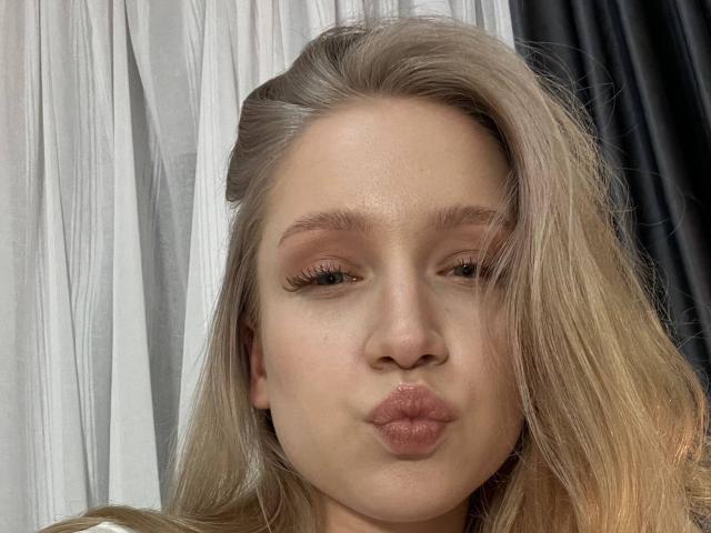 JanellLindinha, con i capelli biondi, le labbra rosa e piene e un trucco leggero, si fa un selfie con le labbra strette. Le sue sopracciglia sono leggermente alzate e ha un'espressione calma..