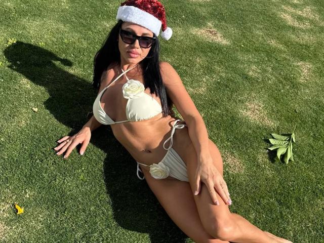 CaseyMin with black hair, wearing a Santa hat, sunglasses, white bikini with yellow rose accents, lying on grass, showcasing her tan skin, small breasts, and trimmed pubic area.
