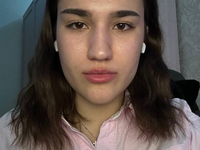 RhondaRump has brown eyes, pink lipstick, and straight brown hair. She's looking at the camera with a slight smirk, resting her hand on her cheek.