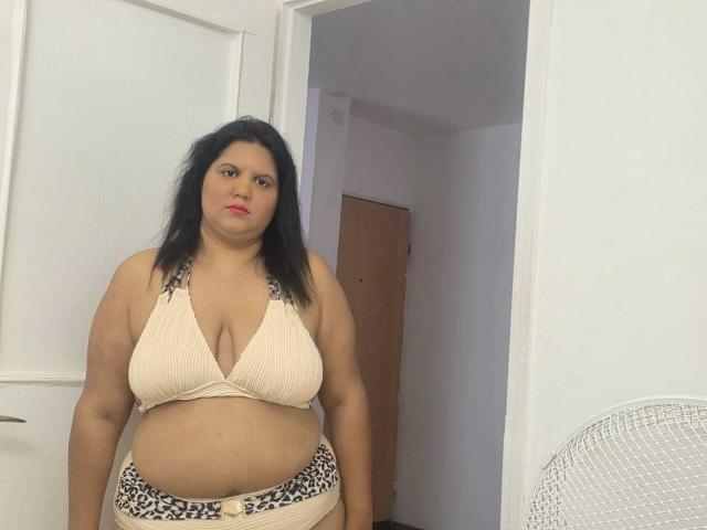 YasminQueen, chubby with tan skin and black hair, wearing a beige ribbed bikini top with leopard print bottoms, standing in a room with a white door and fan.