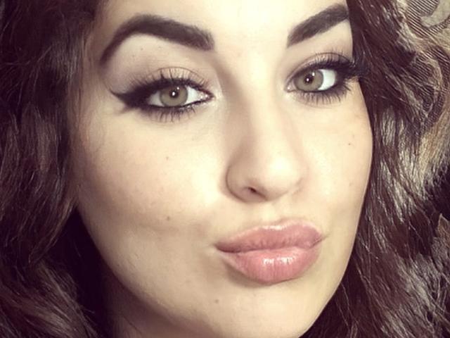 Yzabella69's face, featuring green eyes, thick black eyebrows, long eyelashes, and glossy pink lips. She has wavy dark brown hair and a light skin tone.