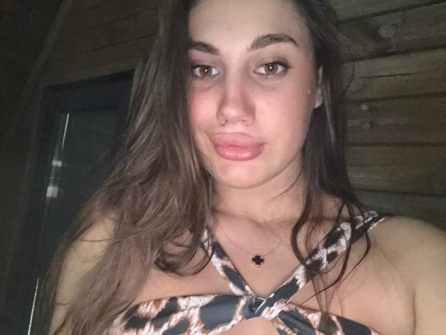ErikaMelody with long brown hair, brown eyes, and pink lips, wearing a leopard print top, showing her small boobs and a black necklace with a star charm.