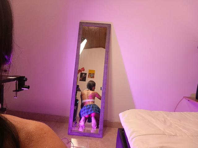CatalellaVercelli kneeling in front of a mirror, wearing a blue plaid skirt, white bra, and pink heels, showing her ass, with her back to the mirror.