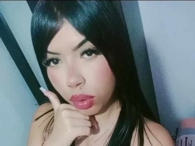 SharlotTeam with dark straight hair, full pink lips, and a nose ring, touching her chin with her finger, looking at the camera with a slight pout.