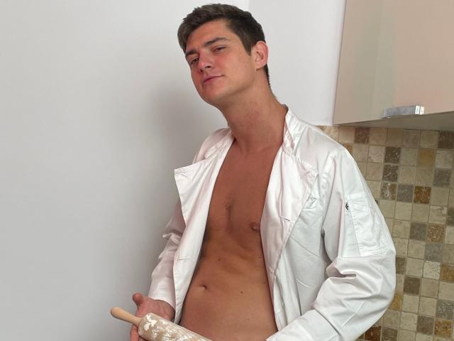 AndyFame, shirtless, white lab coat, holding a wooden spoon, hand in pocket, light skin, short brown hair, slight smile, tiled wall background, muscular, confident.
