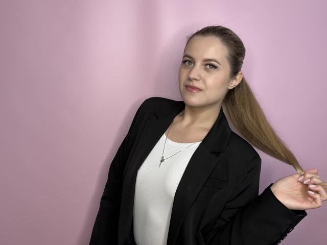 MichaelChaidez has a slender face, light skin, and brown hair in a ponytail, wearing a black blazer over a white top, with a small cross necklace, looking at camera.