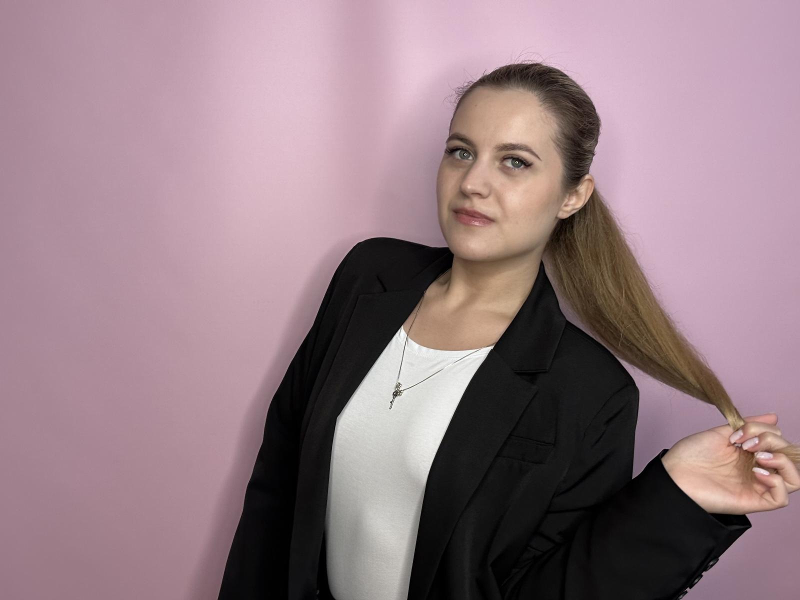 MichaelChaidez has a slender face, light skin, and brown hair in a ponytail, wearing a black blazer over a white top, with a small cross necklace, looking at camera.