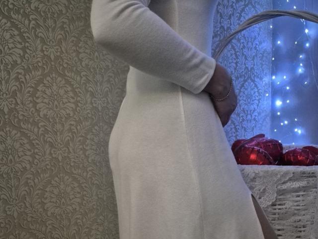 Anshante's white dress hugs her ass, showing a side view with her hand on her hip, standing next to a wicker basket with red ornaments and blue fairy lights.