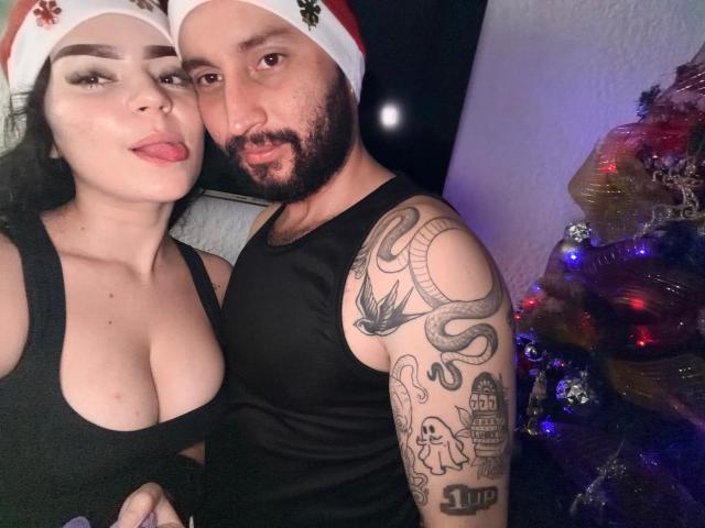 EVAANDWALLE with big tits in a black top, and WALLE with a snake tattoo and beard, both in Santa hats, sticking their tongues out in a Christmas photo.