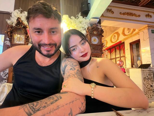 EVAANDWALLE and a guy with tattoos, black tank top, and beard, she's in a black strapless dress, red lipstick, his arm around her, clock and flowers in background.
