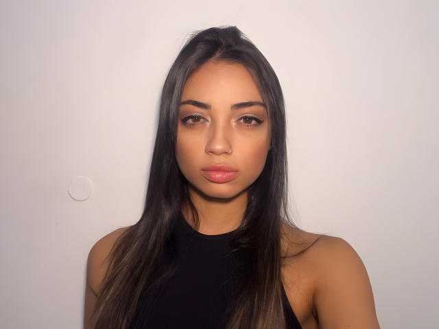 CameliaDeihl has long brown hair, a nose ring, and is wearing a black sleeveless top. Her brown eyes and pink lips are prominent. She's looking directly at the camera.