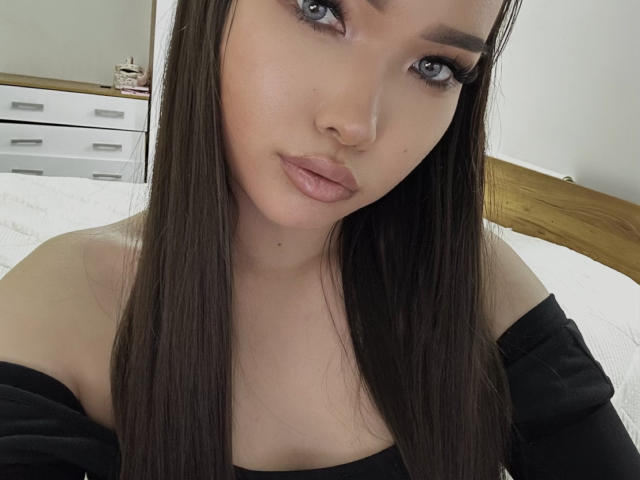 RebecaPfendler has long brown hair, light skin, and is wearing black off-shoulder clothing, showing her tits and pouty pink lips, with blue eyes and subtle makeup.