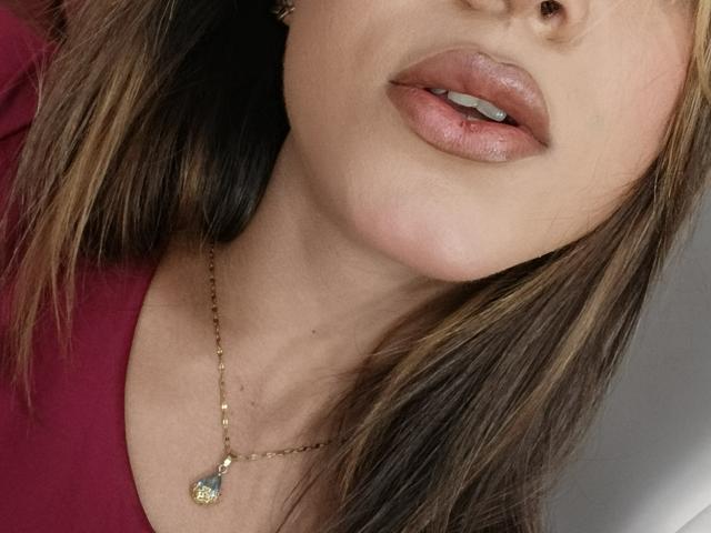 AliceCoolenk's face with glossy pink lips, brown hair with blonde highlights, wearing a gold necklace with a small pendant, and a red top, showing her nose and upper chest.