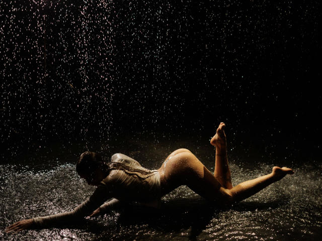 Helena-hot is on all fours, wet, in a dark, water-filled scene. Her ass is up, back arched, water droplets sparkling on her skin. She's wearing a wet, white shirt.