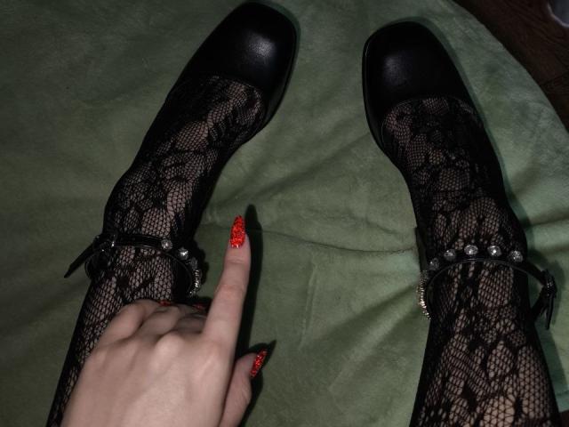Dreia, con i capelli castano ondulati, gli occhi azzurri e una maglia di pizzo nero, morde il dito nero, mostrando i seni attraverso il pizzo. È sexy e la sua sguardo è seducente..