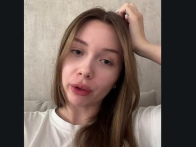SoledadFugo with light brown hair, slightly pouty pink lips, and a white shirt, holding her hair up with one hand, showing a relaxed, casual expression.