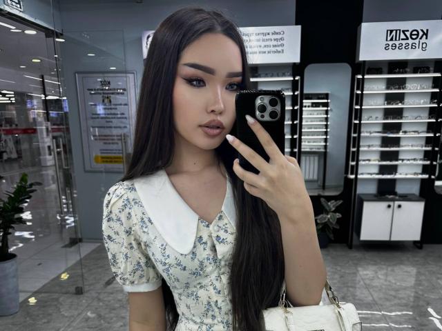 Rebeca Pfendler, met lang zwart haar, draagt een bloemenjurk, houdt een telefoon vast, maakt een selfie, heeft een witte tas in haar hand, kijkt naar de camera, in een moderne winkel, en ziet er aantrekkelijk uit..