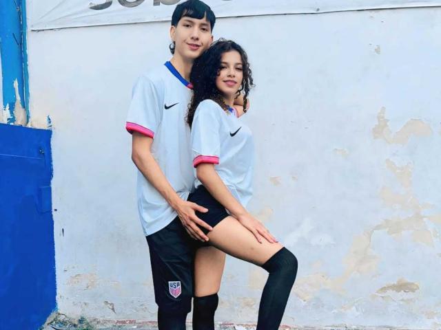 BellainLove with curly dark hair, wearing a white soccer shirt with pink trim, black shorts, and knee socks, has her ass grabbed by BellainLove with black hair.