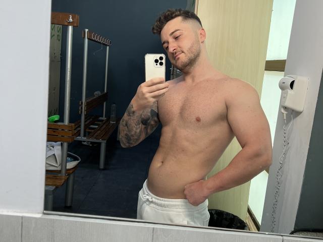 EthannI has a muscular, shirtless, tattooed upper body, white pants, and a short, curly hairstyle. He's taking a mirror selfie with a confident, slightly smug expression.