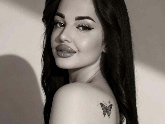 MissJaqueline heeft donker, golvend haar, volle lippen met glanzende lippenstift, en een vlindertatoeage op haar rechter schouder. Ze kijkt over haar schouder met een lichte glimlach..