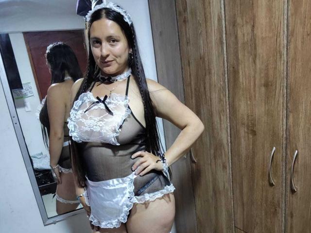 VenusSweetPalmer in a black and white lace maid outfit, sheer top revealing her tits, black ribbon, white frilled apron, and black panties, standing with a hand on her hip.