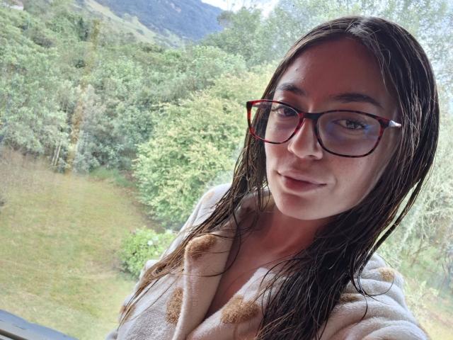 VictoriaPalmerfg with wet brown hair, wearing glasses, and a white robe, showing her tits in a selfie, looking at the camera with a slight smile.