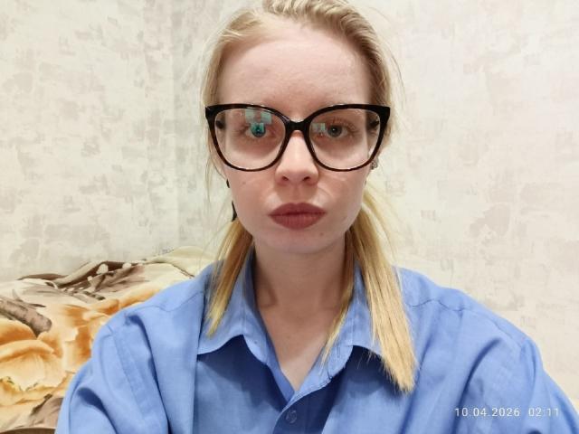 TemekaTrick with blonde hair, black glasses, and pouty lips, wearing a blue shirt, has a serious expression, and a date stamp in the bottom right.
